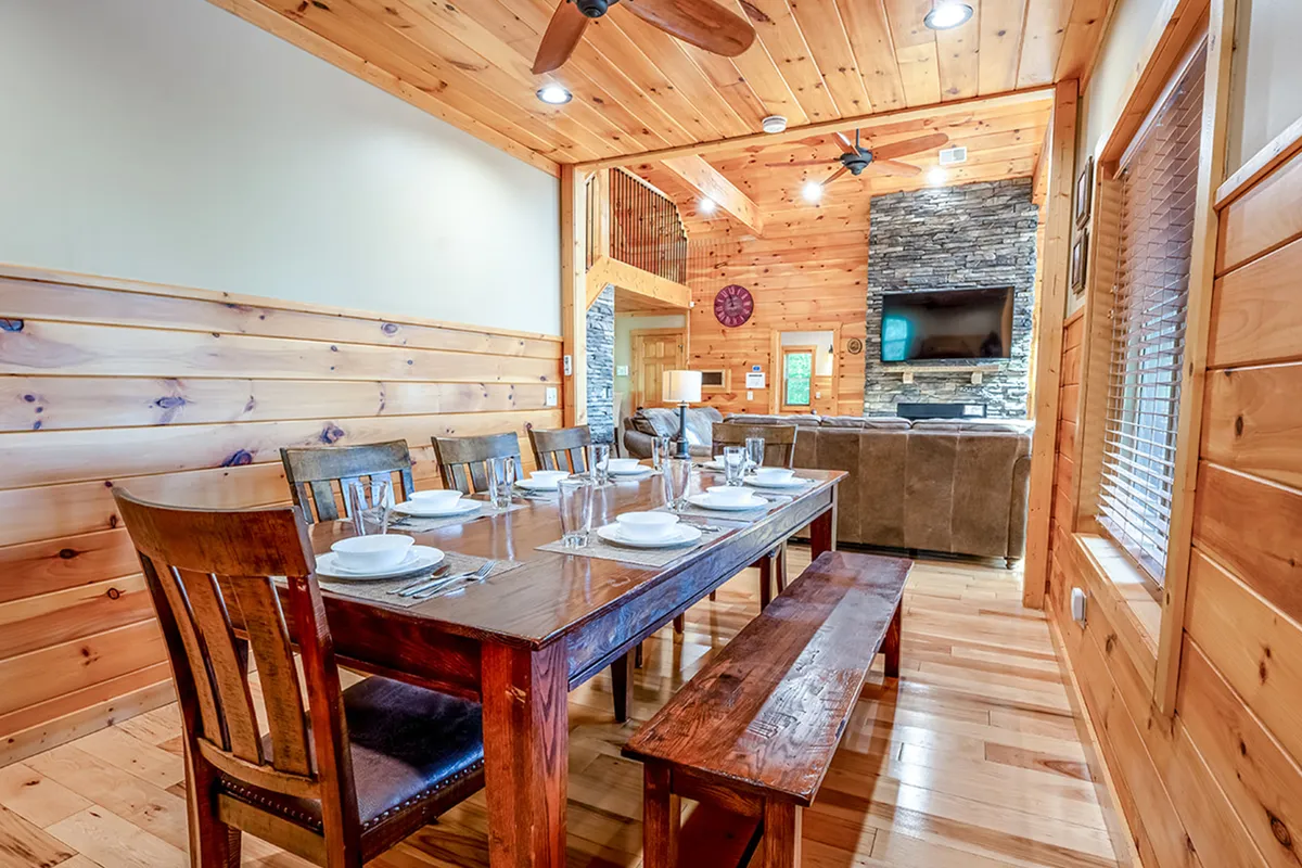 A cozy dining area adjacent to a stone fireplace, featuring a wooden dining table with chairs, perfect for family meals, game nights, or group celebrations. The space feels warm and welcoming, ideal for shared dining experiences.
