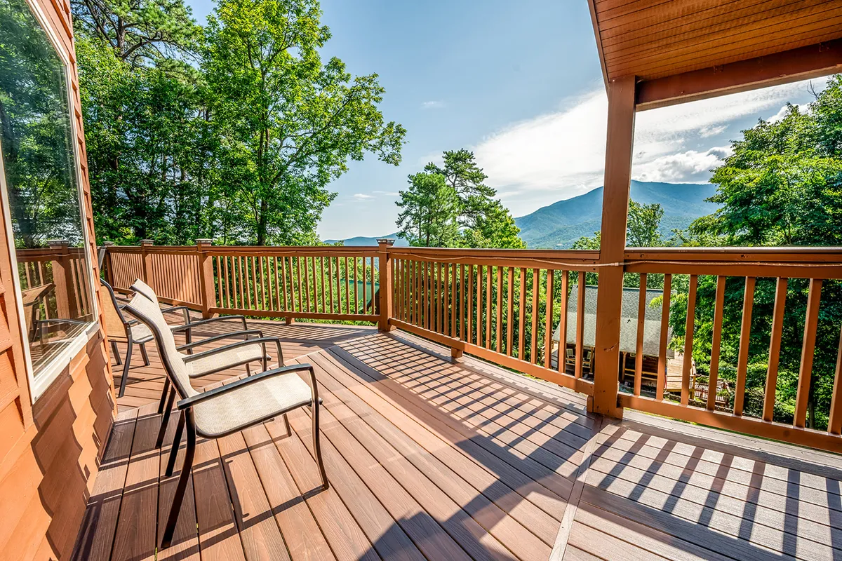 A serene wooden deck furnished with outdoor chairs, overlooking expansive mountain views. The deck is surrounded by lush greenery, offering a panoramic perspective of the Smoky Mountains and providing a direct connection to the surrounding nature.