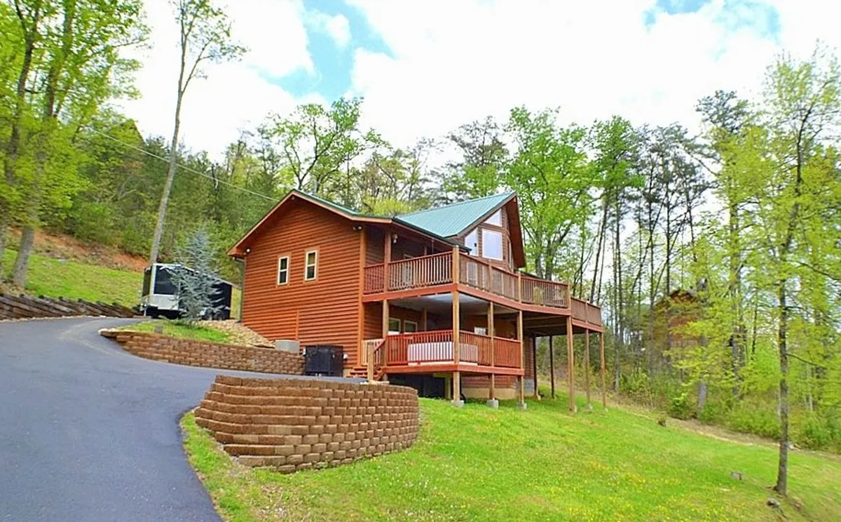 A welcoming view of Bearmont Lodge’s wooden exterior, featuring a spacious balcony, landscaped yard, and driveway. The image captures the inviting porch and hints at the space available for group gatherings and outdoor enjoyment, set against a backdrop of lush greenery.