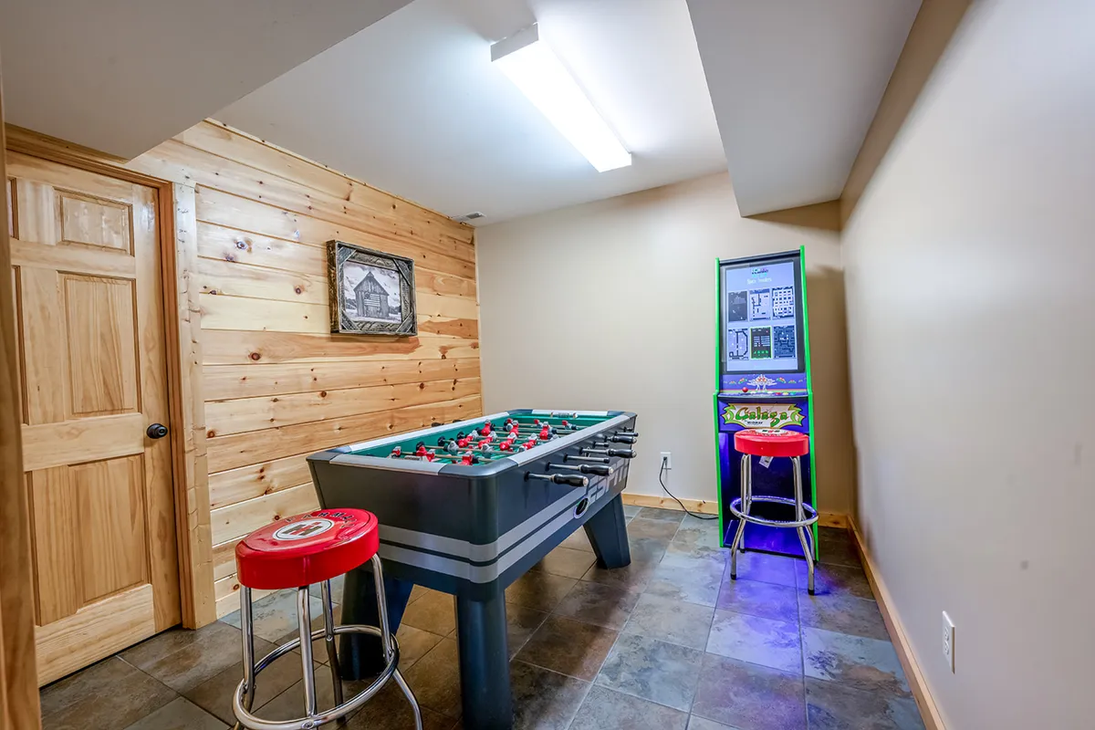 A lively area with a foosball table and arcade game machine, complemented by bar stools and playful wooden panel wall art. The space is designed for interactive fun, ideal for tournaments and arcade challenges among guests. The setup encourages both group activities and individual play.