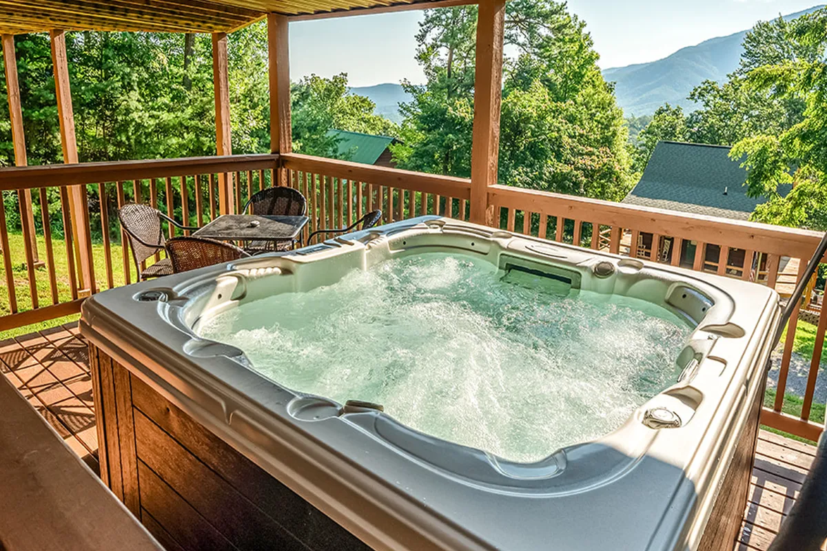 An exterior shot of the deck area featuring a bubbling hot tub, outdoor seating, and panoramic mountain views. The tranquil setting invites relaxation and socializing while immersed in nature.