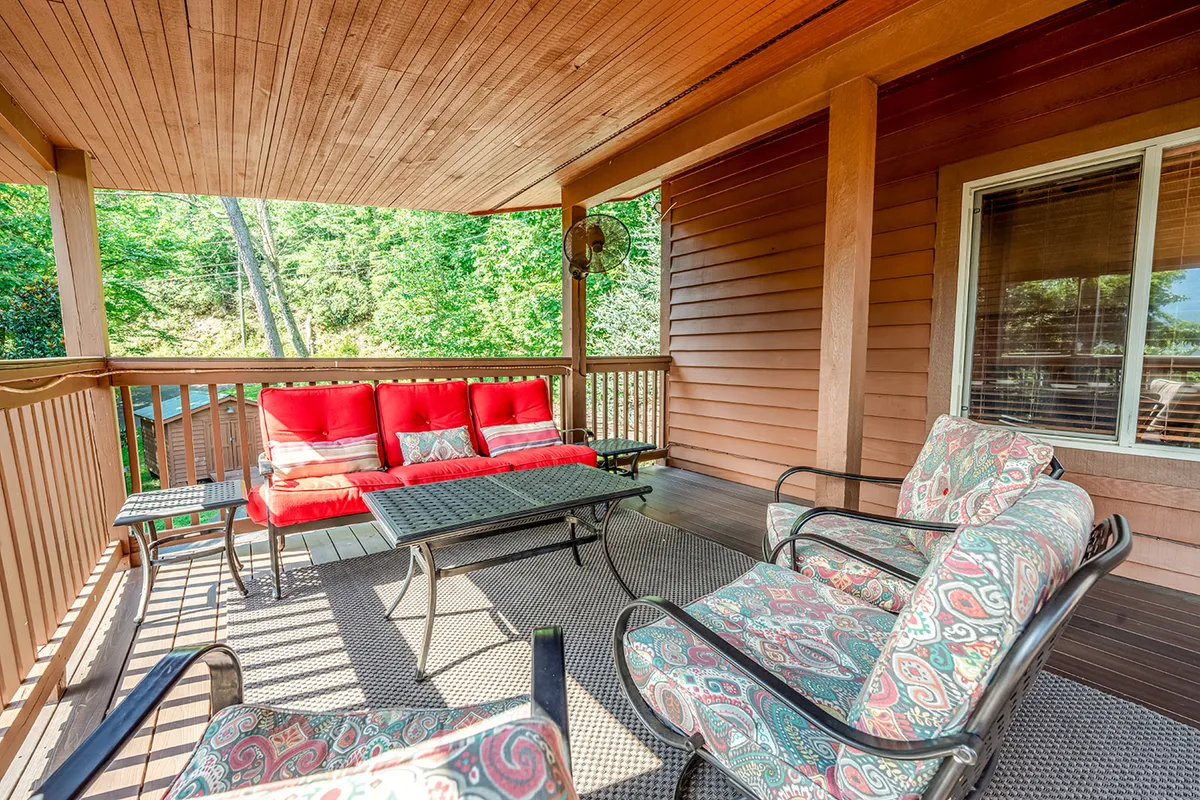 A comfortable porch set with a red sofa, decorative chairs, a glass coffee table, and wooden railing overlooking nature. The space radiates comfort and is perfect for relaxing conversations, morning coffee, or planning the day’s adventures.