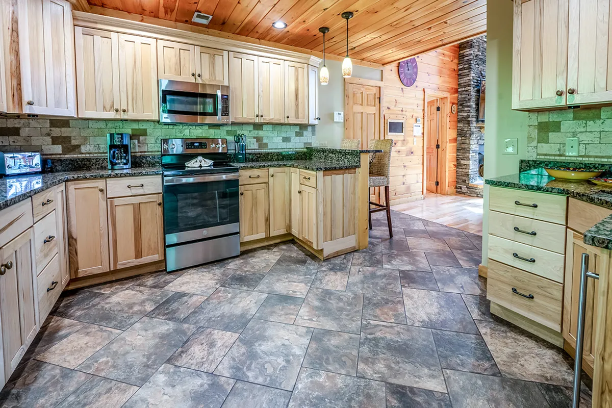 A warm and inviting kitchen featuring granite countertops, stainless steel appliances, wooden cabinetry, and a stone wall accent. The layout is open and spacious, perfect for group cooking and entertaining.