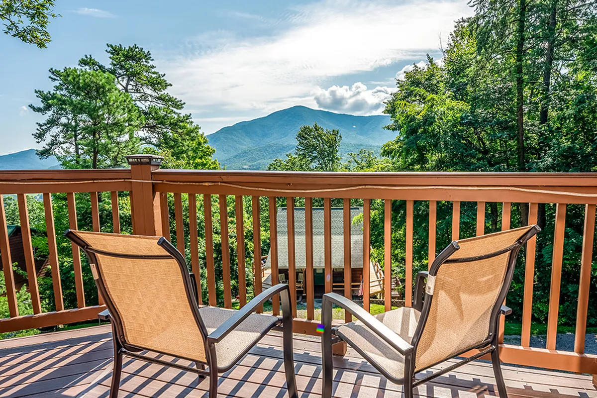 A rustic deck with wooden railings and comfortable chairs, offering panoramic views of the mountains. The peaceful outdoor space is ideal for gathering, stargazing, or enjoying morning coffee together, surrounded by nature.