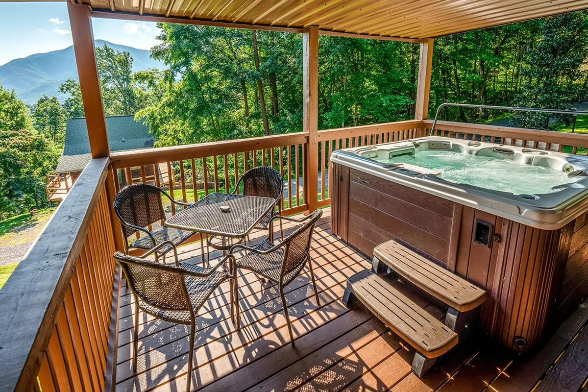An inviting hot tub sits on a deck overlooking sweeping mountain views. The outdoor seating area nearby is ideal for relaxation or group conversations, all set against the tranquil backdrop of the Smoky Mountains. The setting is perfect for unwinding after a night out.