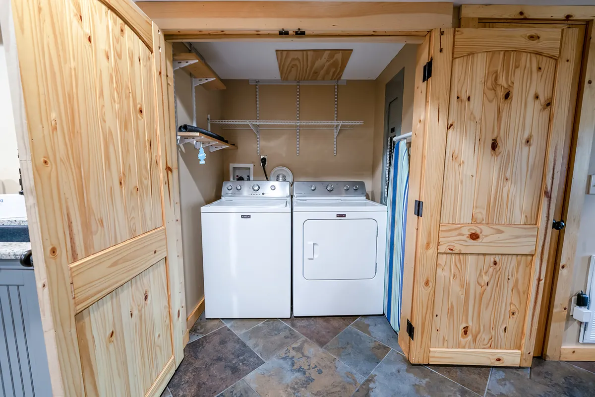 A practical laundry nook with a washing machine, dryer, wooden doors, and a shelving unit. The clean, organized setting ensures guests can keep up with laundry during longer stays, adding convenience to the fun-focused environment.